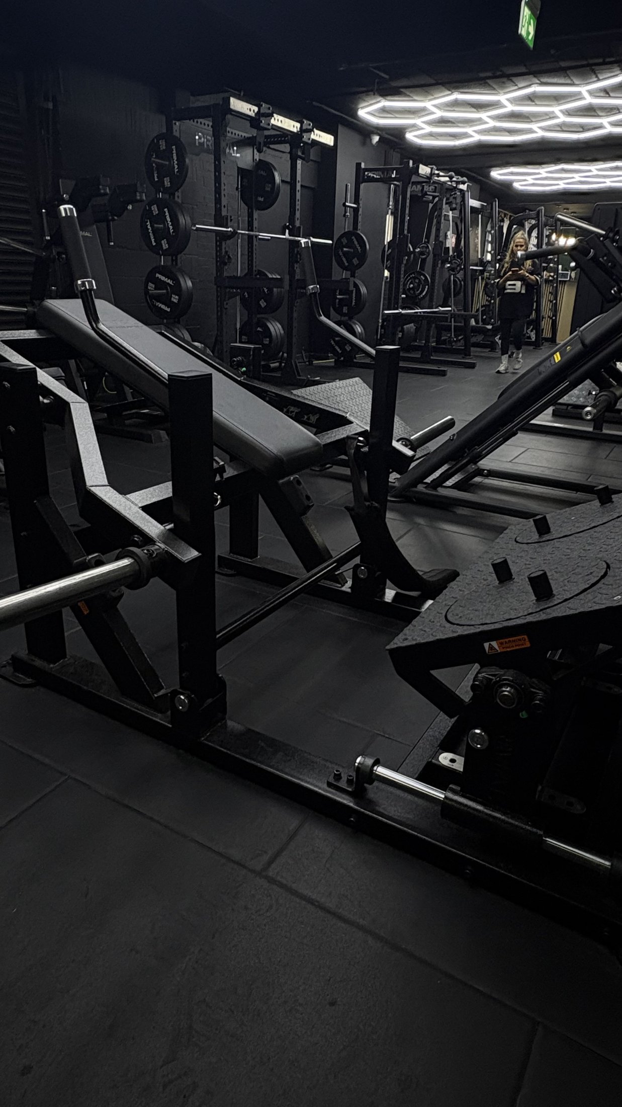 Bench press stations and leg press with Olympic weight plates on the gym floor