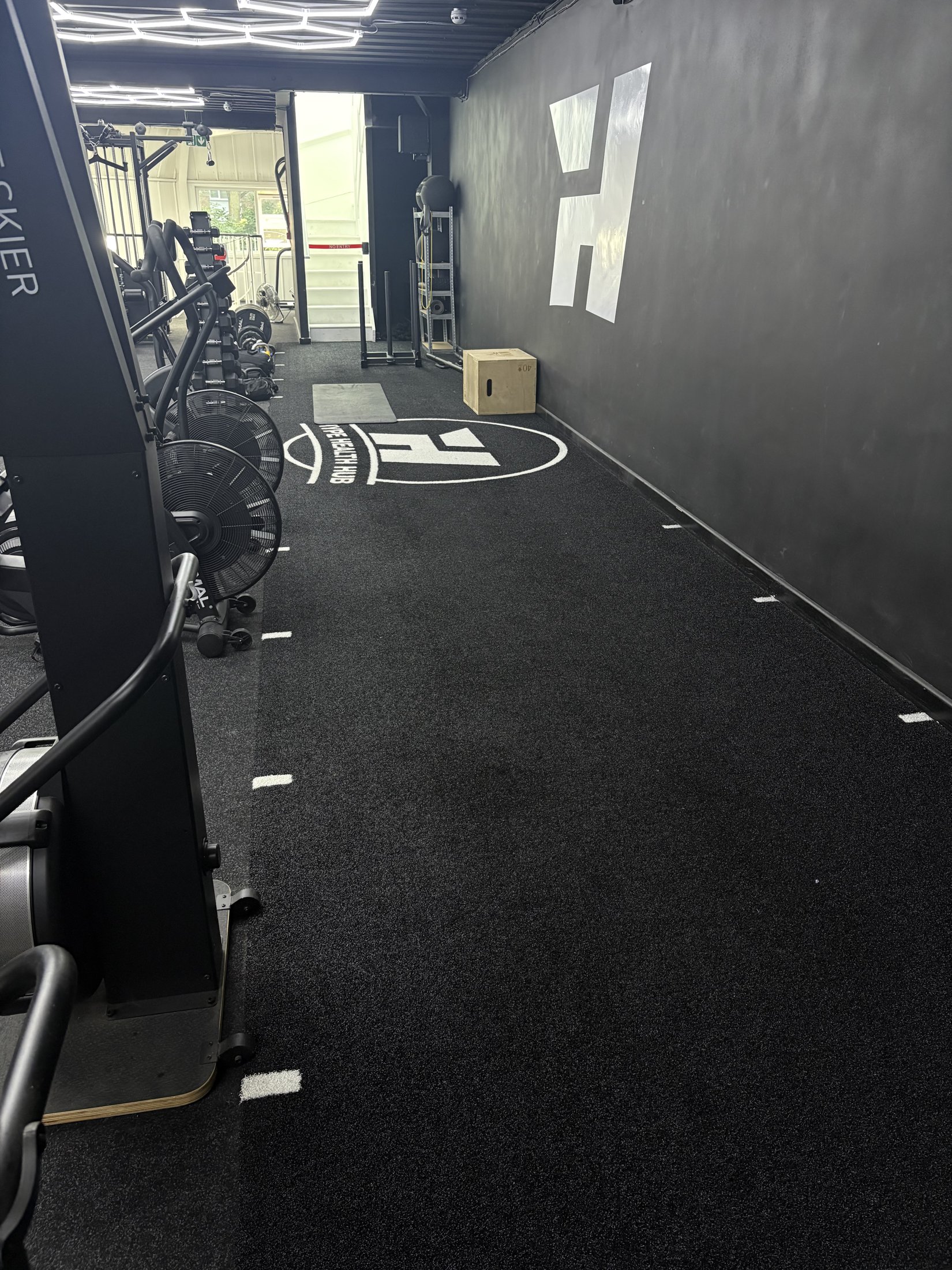Functional turf training lane with sled track, plyo box and StairMaster cardio machines beside the Hype Gym wall logo